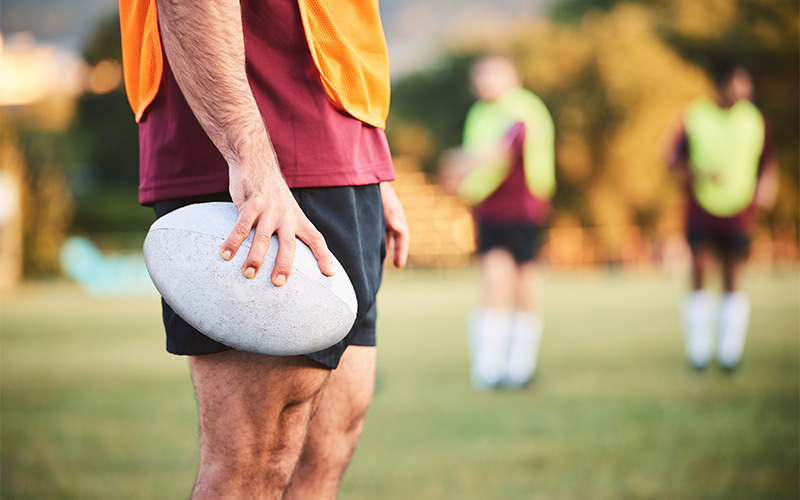 Athlete holding a rugby ball on the sports field.