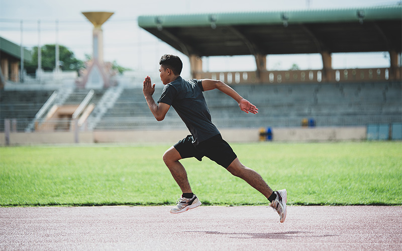 Male runner sprinting on track risking proximal hamstring tendinopathy.